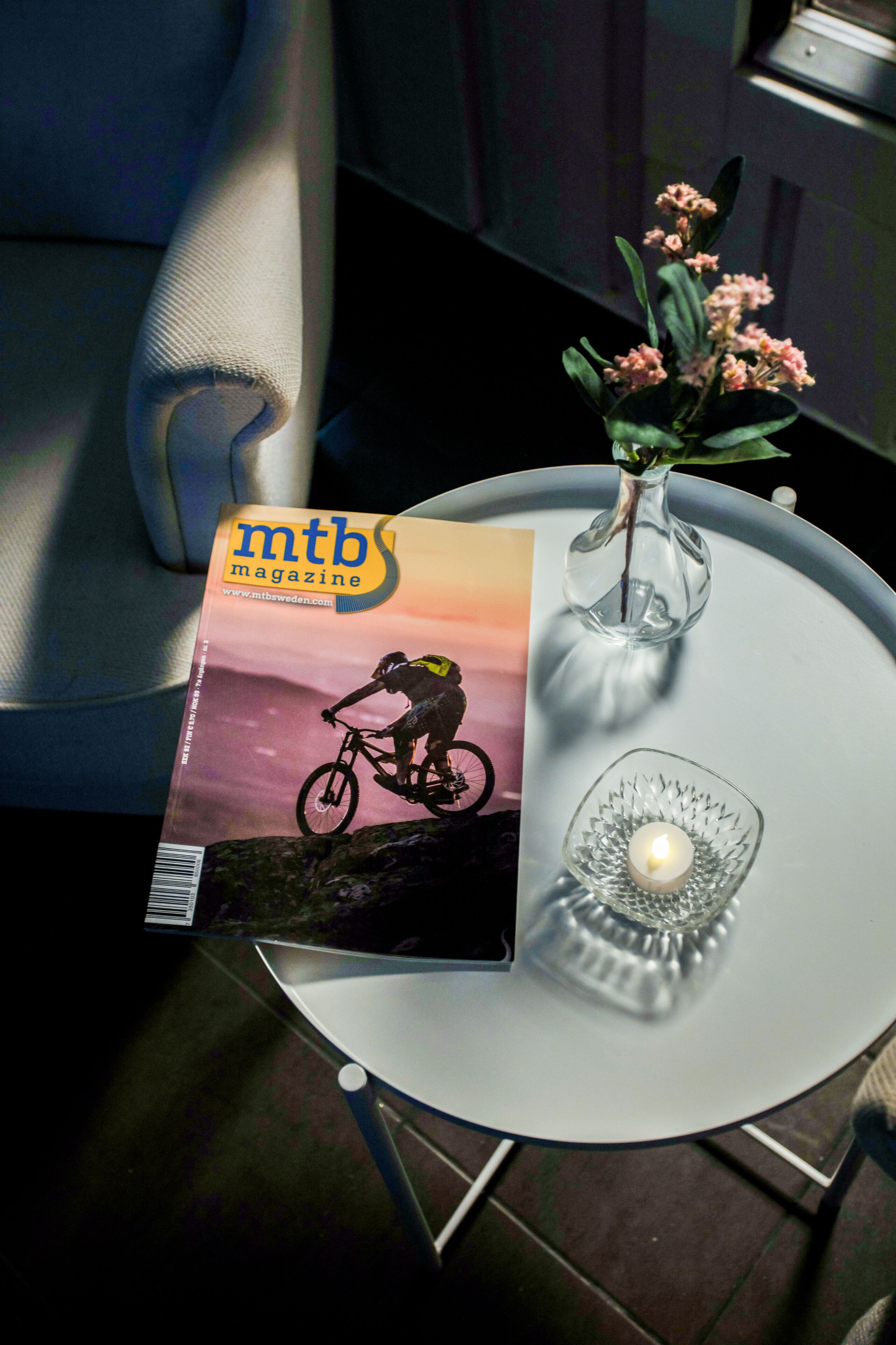 A magazine on a table, a candle, and a vase with flowers.