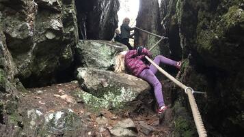 A person lying on a rope bridge in a rocky, forested area.