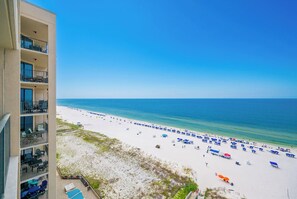 A beach with umbrellas and lounge chairs, a clear blue sky, and a building with balconies.