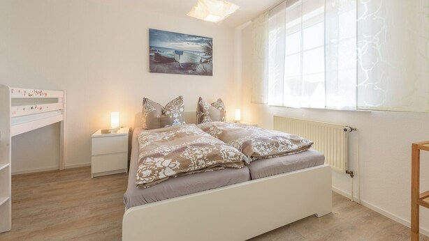 A bedroom with a bed, bedside tables, a nightstand, a window with sheer curtains, and a painting on the wall. - Apartment in Prerow up to 2 p. + child up to 6 y., quiet, close to the beach, parking lot, WLAN (Prerow)