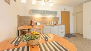 A modern kitchen with wooden cabinets, a dining table with a fruit basket, and a striped rug. - Apartment in Prerow up to 2 p. + child up to 6 y., quiet, close to the beach, parking lot, WLAN (Prerow)
