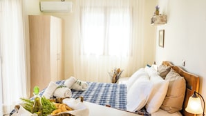 A hotel room with a bed, a bedside table with a lamp, a window with sheer curtains, and a wall-mounted air conditioner.