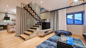 Una sala de estar moderna con una escalera de cristal, un televisor de pantalla plana, un sofá y un comedor con mesa y sillas.