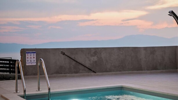 Una piscina en la azotea con vistas a montañas, una pared de concreto y una baranda de metal.