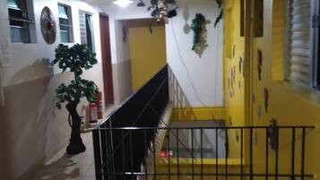Uma escadaria com parede amarela, corrimão preto e piso de azulejos.