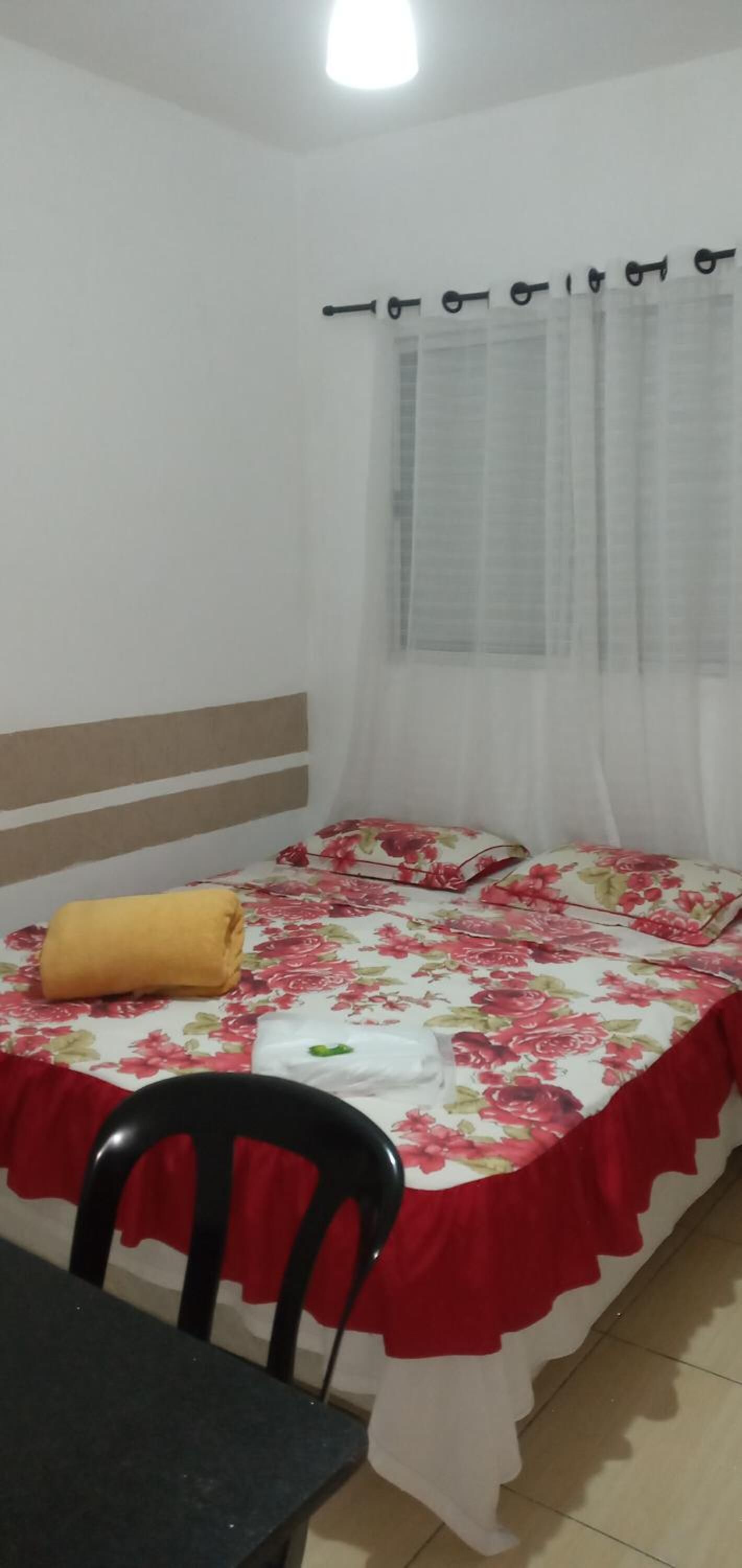 Un dormitorio con cama, una silla y una ventana con cortinas.