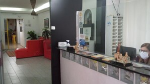 Una zona de recepció amb un taulell negre, seients vermells i una paret blanca amb un rellotge i un senyal.