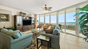A spacious living room with a large window overlooking the ocean, a ceiling fan, and a variety of seating options. - Three Bedroom Condo with Lazy River & Gulf of Mexico Views. Complimentary Boat Slip! (Orange Beach)