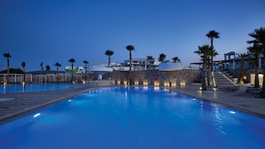 Una piscina con muro de piedra y palmeras, rodeada de edificios modernos.