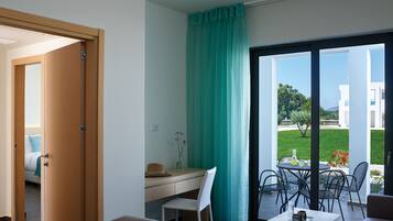 A modern room with a desk, a chair, a table with a vase, and a view of a garden and buildings outside.