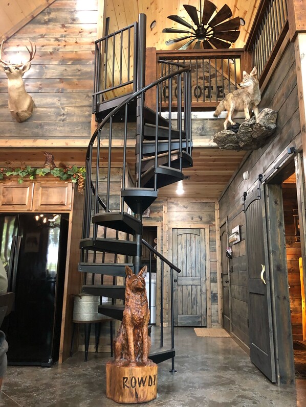 Een wenteltrap in een rustiek interieur met houten wanden, een opgehangen hertenkop, een wolfbeeld en een windmolenornament.