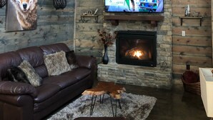 Una sala de estar acogedora con chimenea de piedra, un sofá de cuero, un televisor montado en la pared y un ventilador de techo.