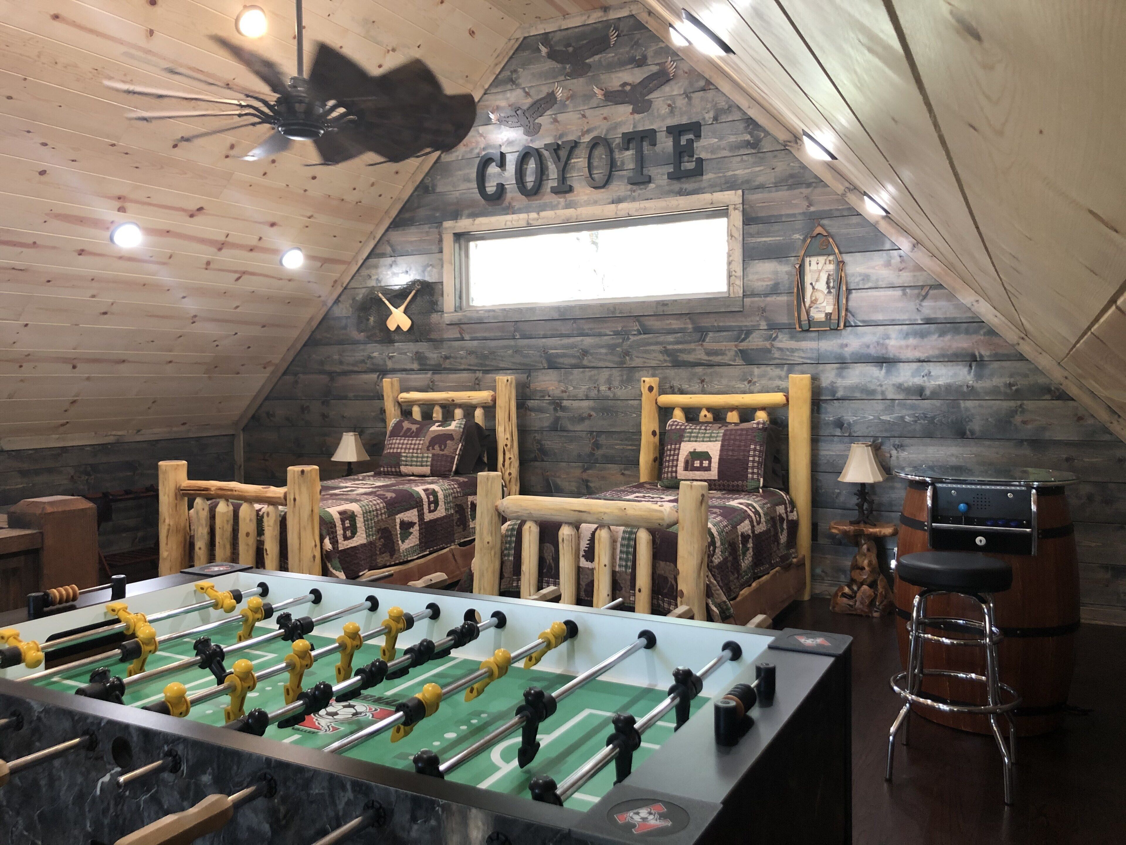 A cozy room with two wooden beds, a foosball table, and a rustic wooden ceiling.