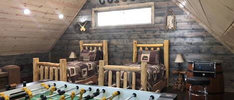 A cozy room with two wooden beds, a foosball table, and a rustic wooden ceiling.