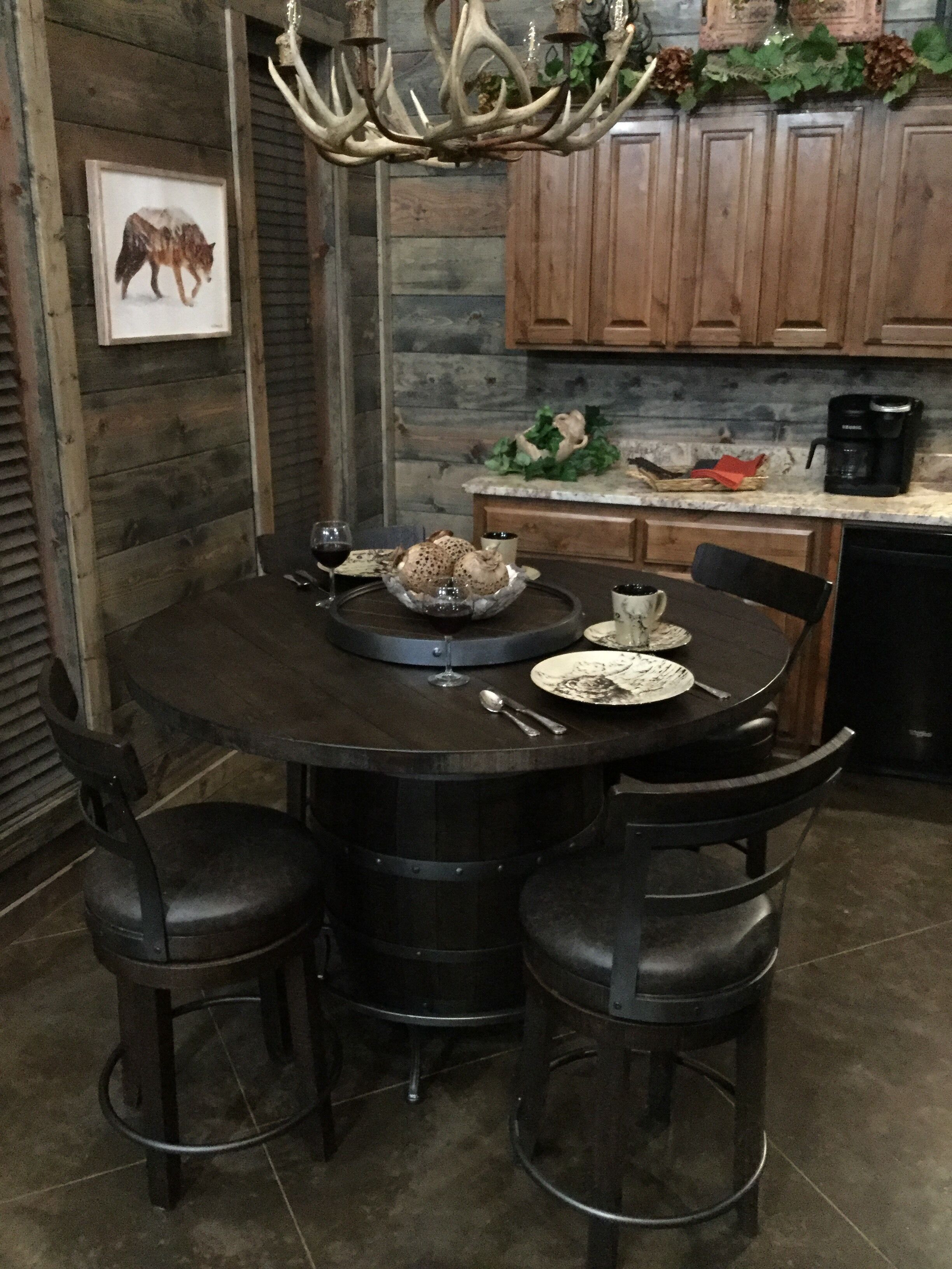 Un coin repas rustique avec une table ronde, quatre chaises, un lustre et une cuisine en arrière-plan.