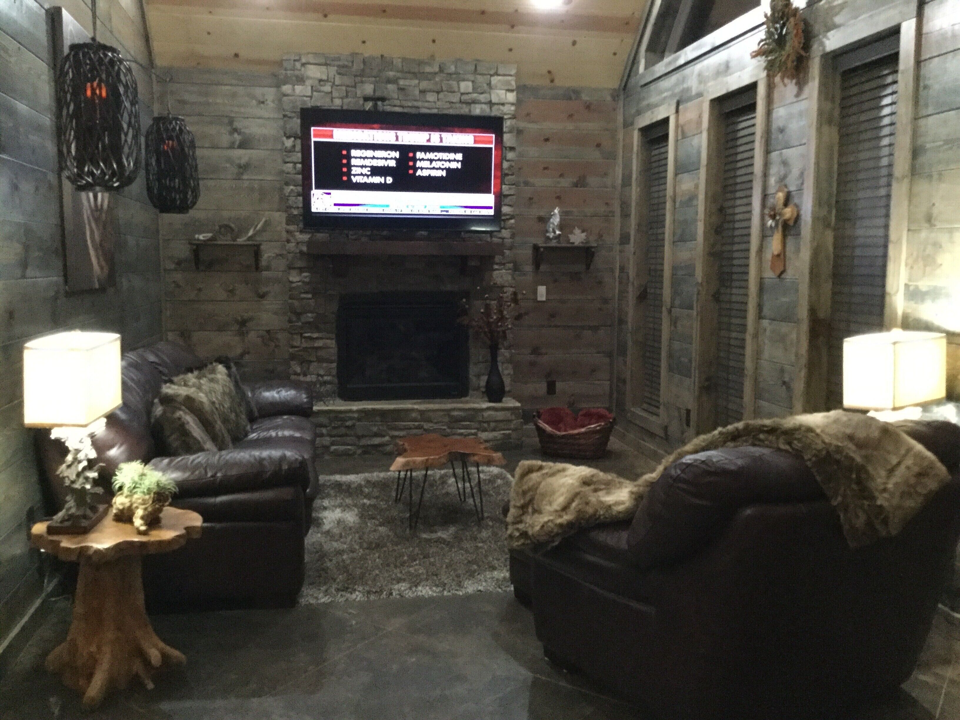 Ein gemütliches Wohnzimmer mit Kamin aus Stein, Ledersofas und einem flachbildfernseher, der darüber angebracht ist.