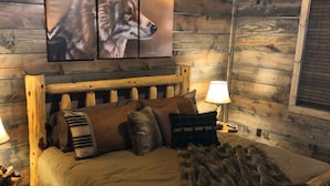 Un dormitorio rústico de madera con cama, almohadas, una colcha y un cuadro colgado en la pared de un lobo.