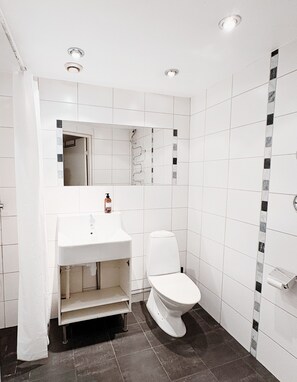 A modern bathroom with white tiles, a white sink, and a toilet. - Hotel Lemonade (Gothenburg)