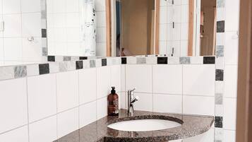 A bathroom with a white sink, a mirror, and a bottle of shampoo.