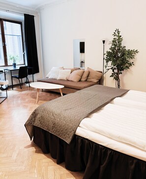 A modern room with a bed, a sofa, a small round table, a potted plant, and a window with curtains. - Hotel Lemonade (Gothenburg)