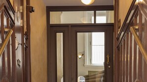 Una escalera con peldaños alfombrados que conduce a una puerta de madera oscura con paneles de vidrio.