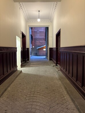 A hallway with a brick floor, wooden paneling on the walls, and a ceiling light. - Hotel Lemonade (Gothenburg)
