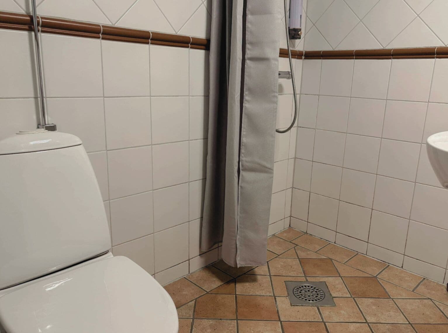 Un baño con azulejos blancos, una cortina de ducha, un inodoro y un lavabo.