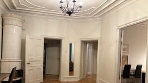 Una habitación amplia con piso de madera, paredes blancas y una araña. Hay dos puertas que dan a otras habitaciones, y un comedor con mesa y sillas.