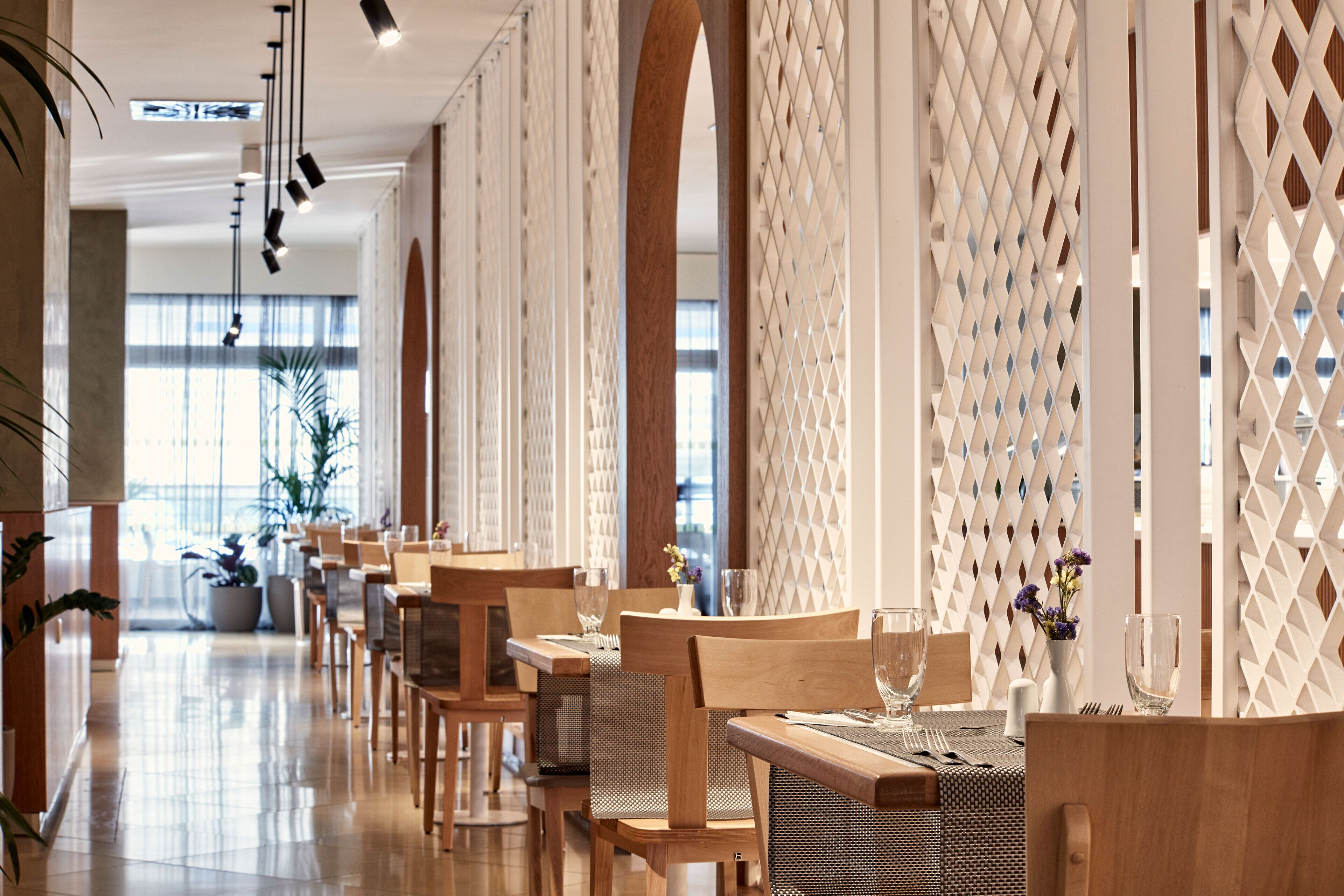 A modern dining area with wooden tables and chairs, a decorative lattice wall, and potted plants.