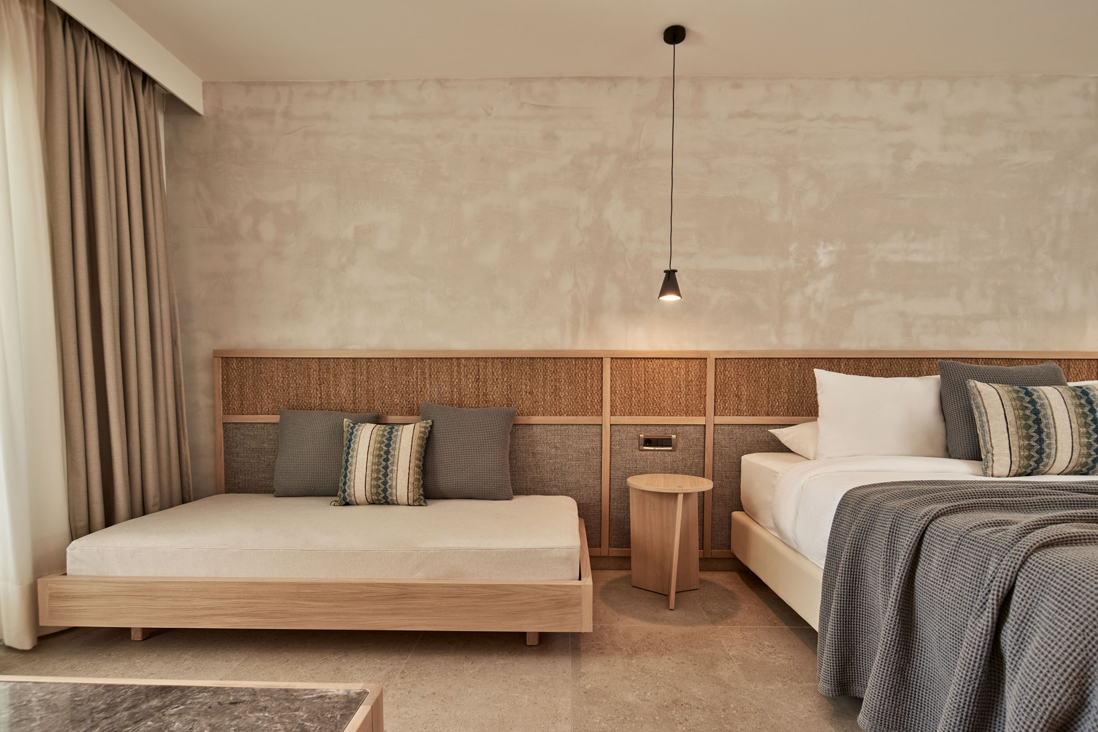 Una habitación de hotel moderna con una cama grande, una cama más pequeña, una mesita redonda y una lámpara colgante.