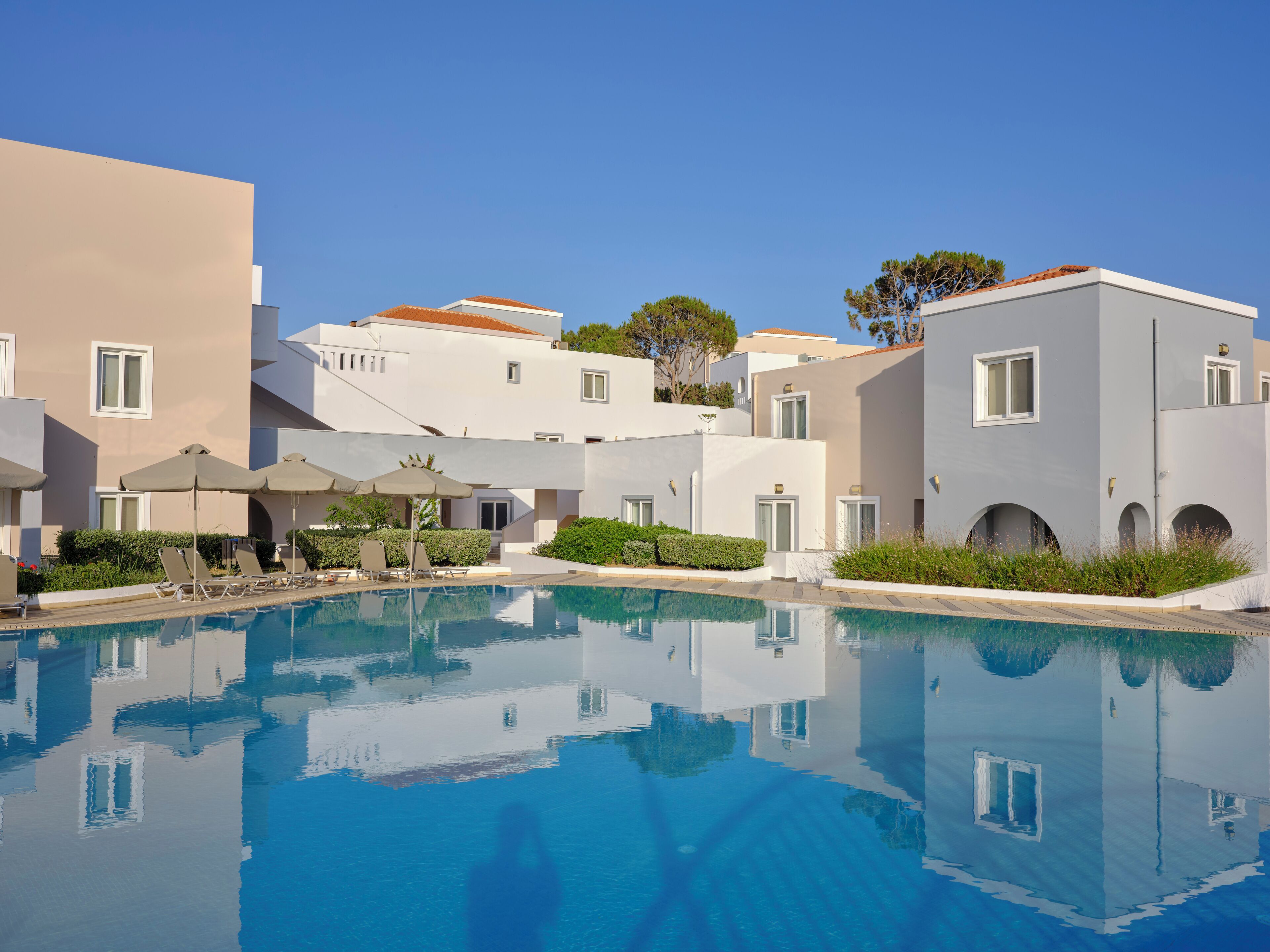 A pool area with lounge chairs and umbrellas, surrounded by modern buildings with balconies and windows.