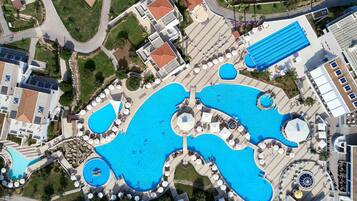 An aerial view of a resort with multiple swimming pools, sun loungers, and a central circular water feature.