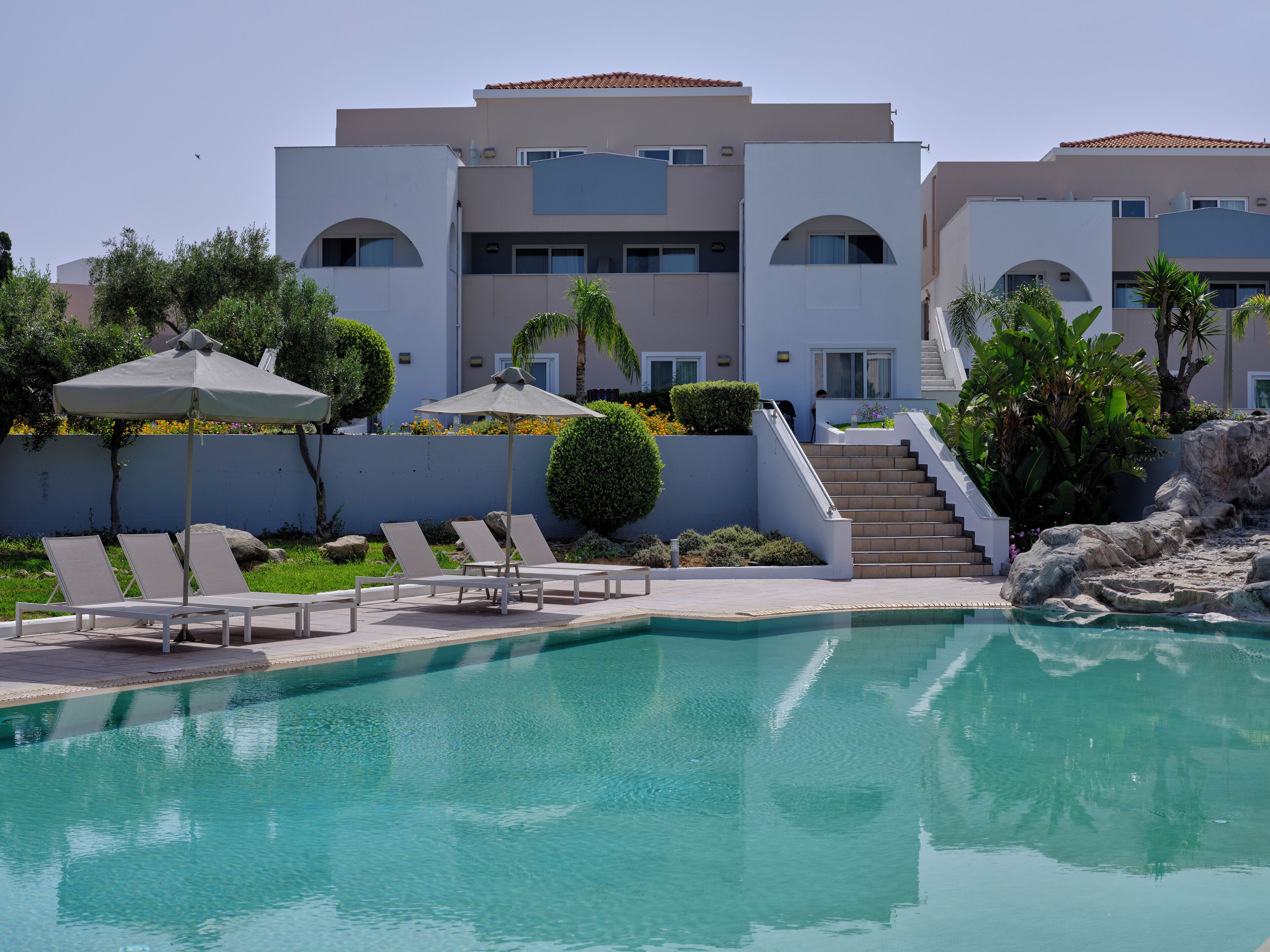 A modern hotel with a pool area, including lounge chairs and umbrellas.