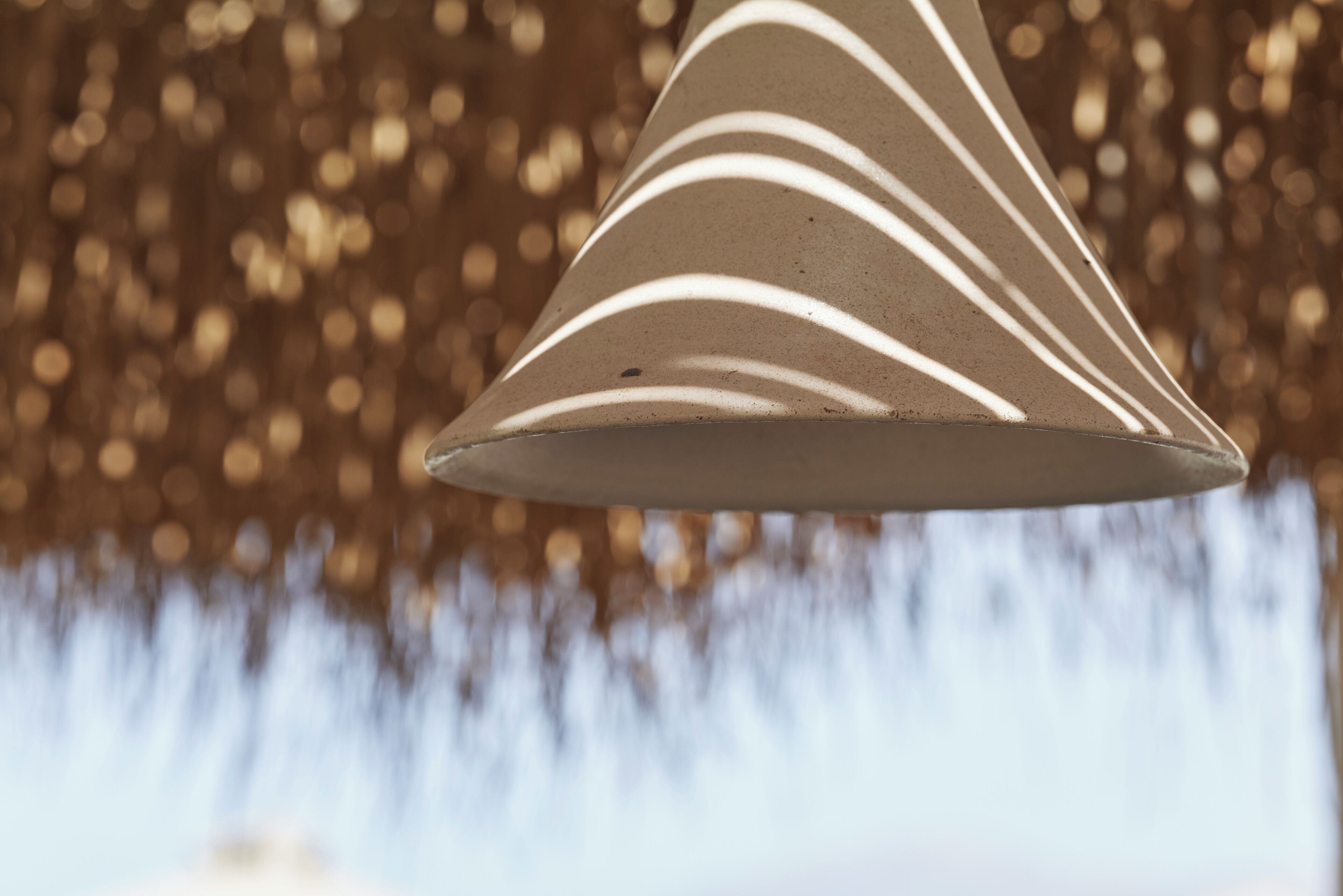 A conical light fixture with a patterned design, set against a blurred background.