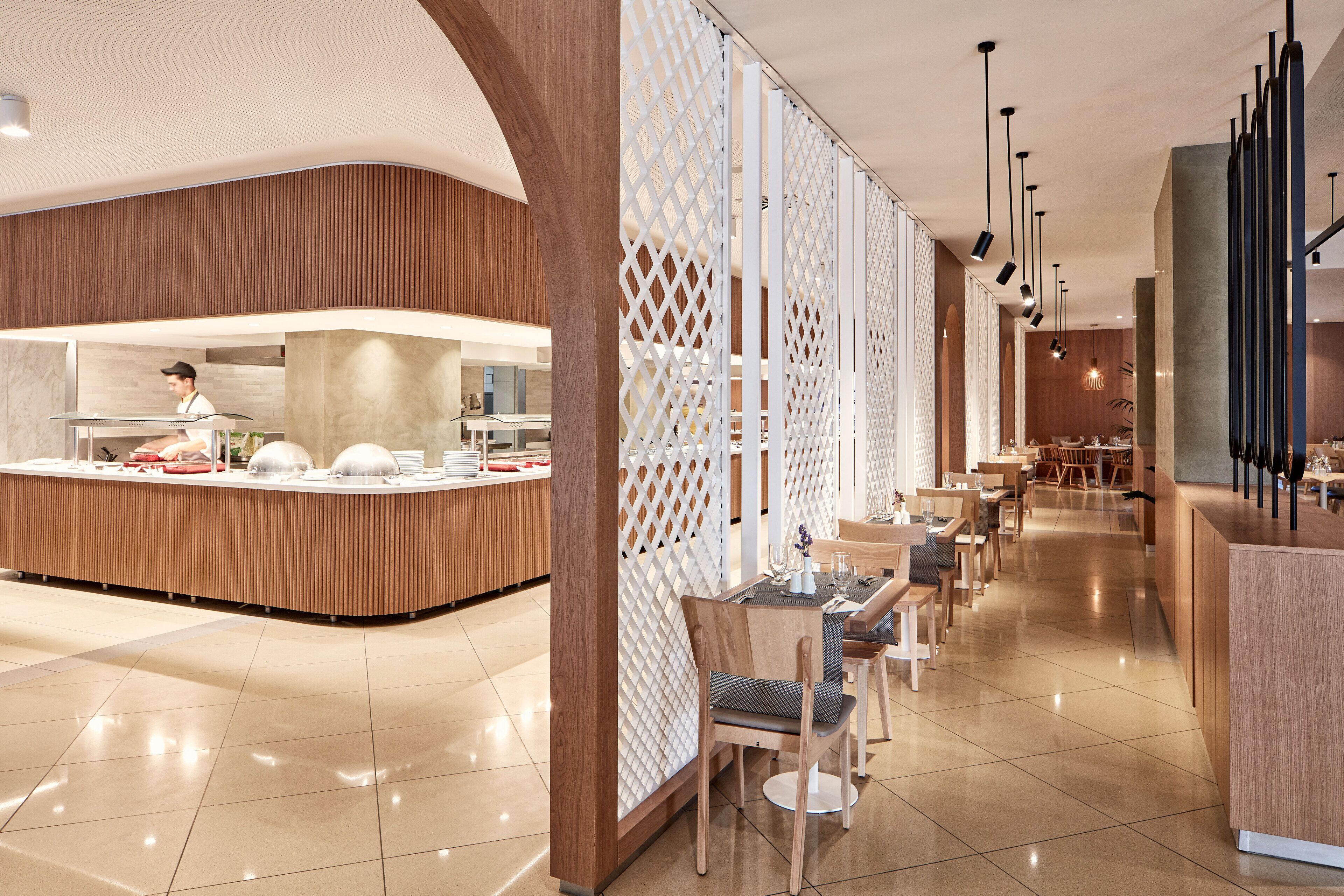 A modern hotel lobby with a reception desk, a dining area, and a bar.