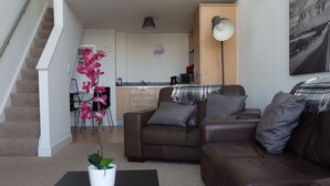En lägenhet i två våningar med en trappa, ett matområde, ett kök och ett vardagsrum med en brun lädersoffa, ett svart soffbord och en orkidé i en kruka.