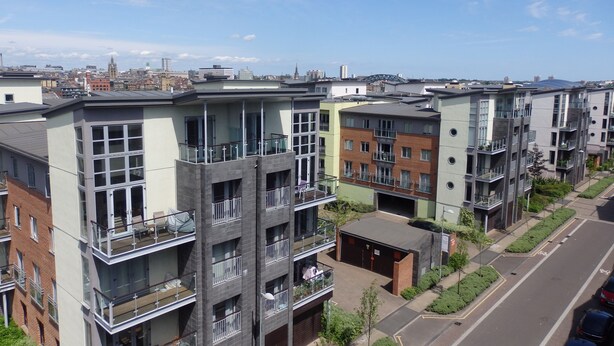 En flervåningsbyggnad med bostäder, balkonger, en parkeringsplats och fri utsikt över stadens silhuett i bakgrunden.