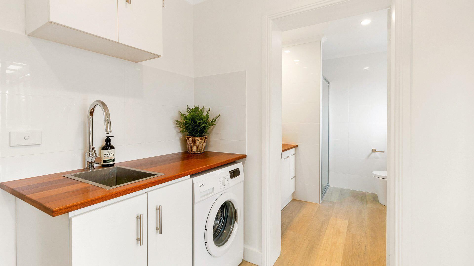 Cocina moderna con armarios blancos, encimera de madera, lavadora y un lavamanos con grifo.