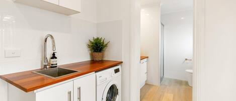 Cocina moderna con armarios blancos, encimera de madera, lavadora y un lavamanos con grifo.