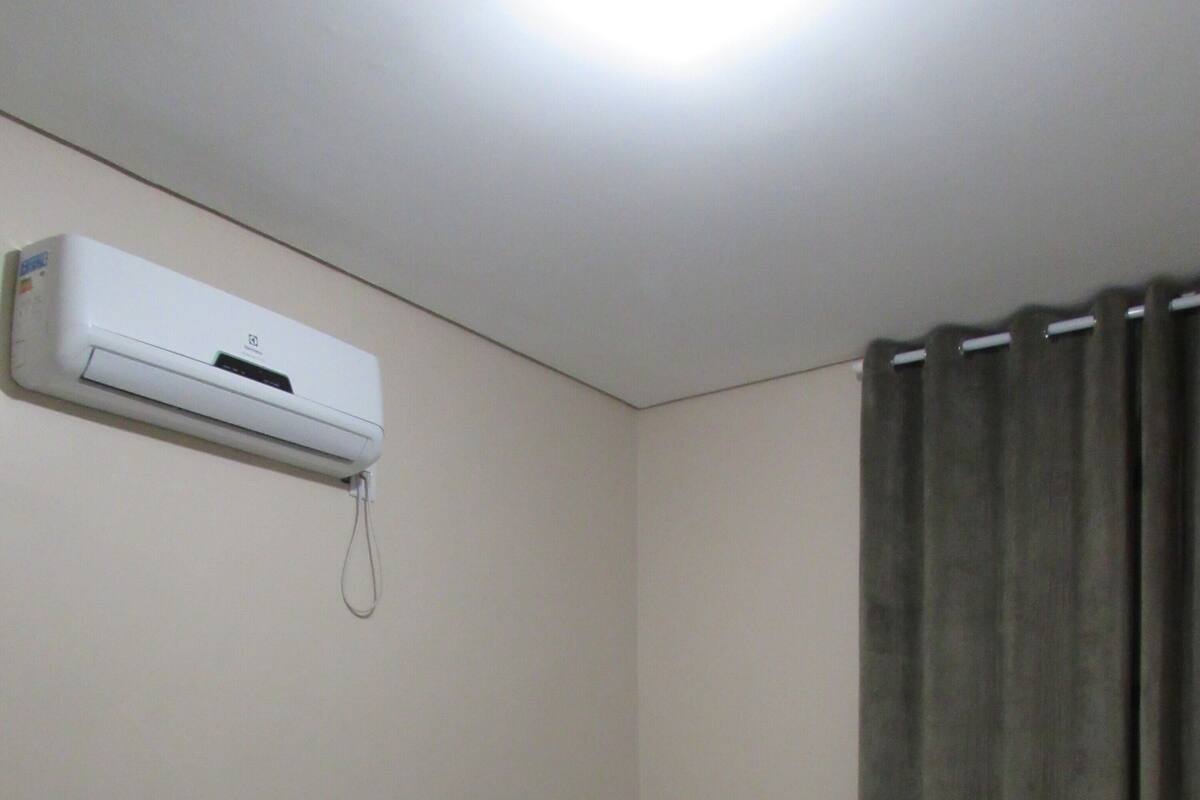 Una cama individual con una colcha azul y blanca a rayas, un almohadón blanco y un aire acondicionado instalado en la pared.