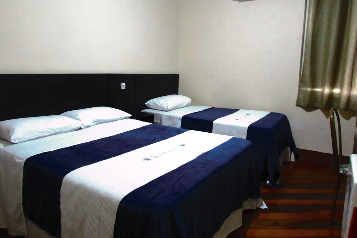 Habitación de hotel con dos camas, cabeceros, mesitas de noche, lámparas y una ventana con cortinas.