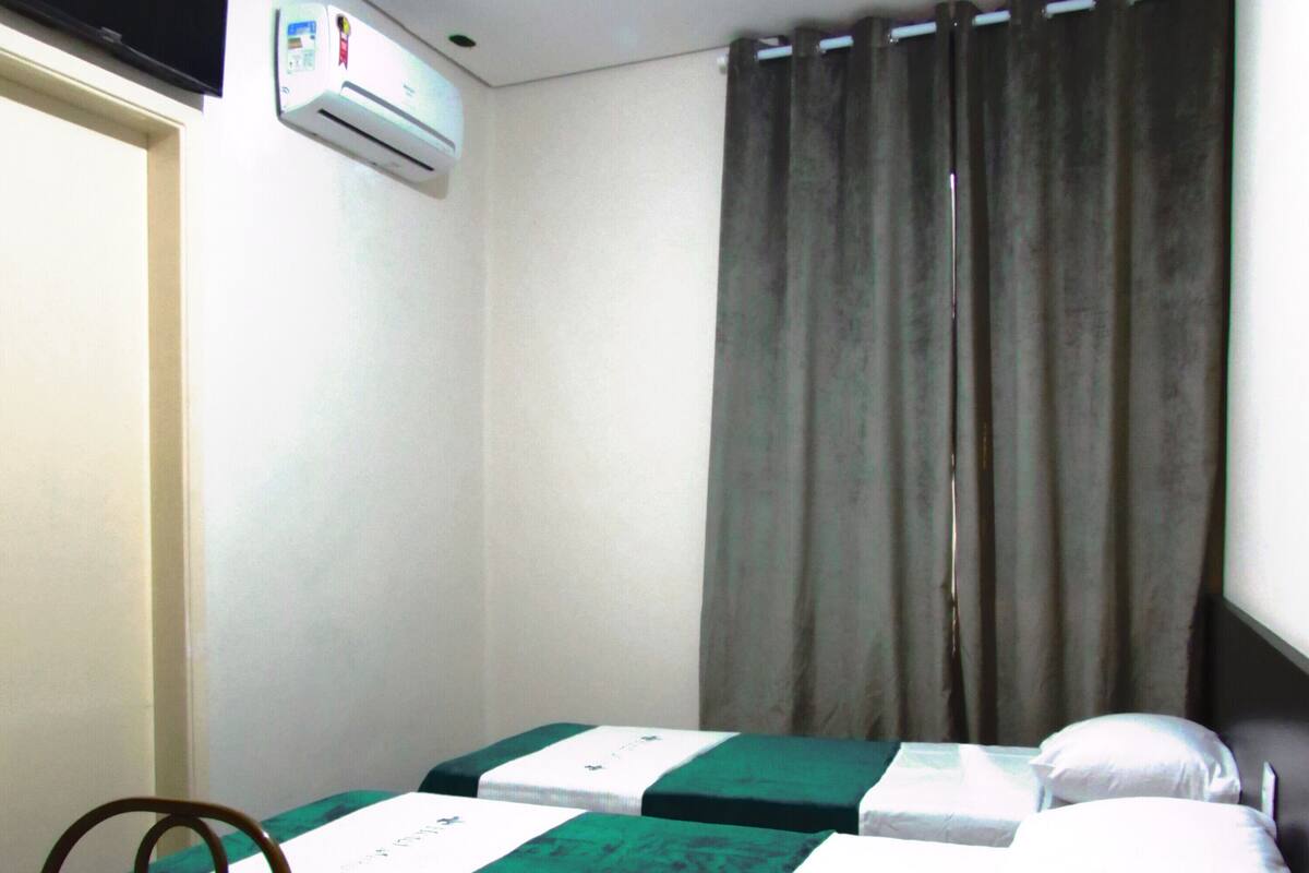 Habitación de hotel con dos camas individuales, un escritorio, una silla y un equipo de aire acondicionado.