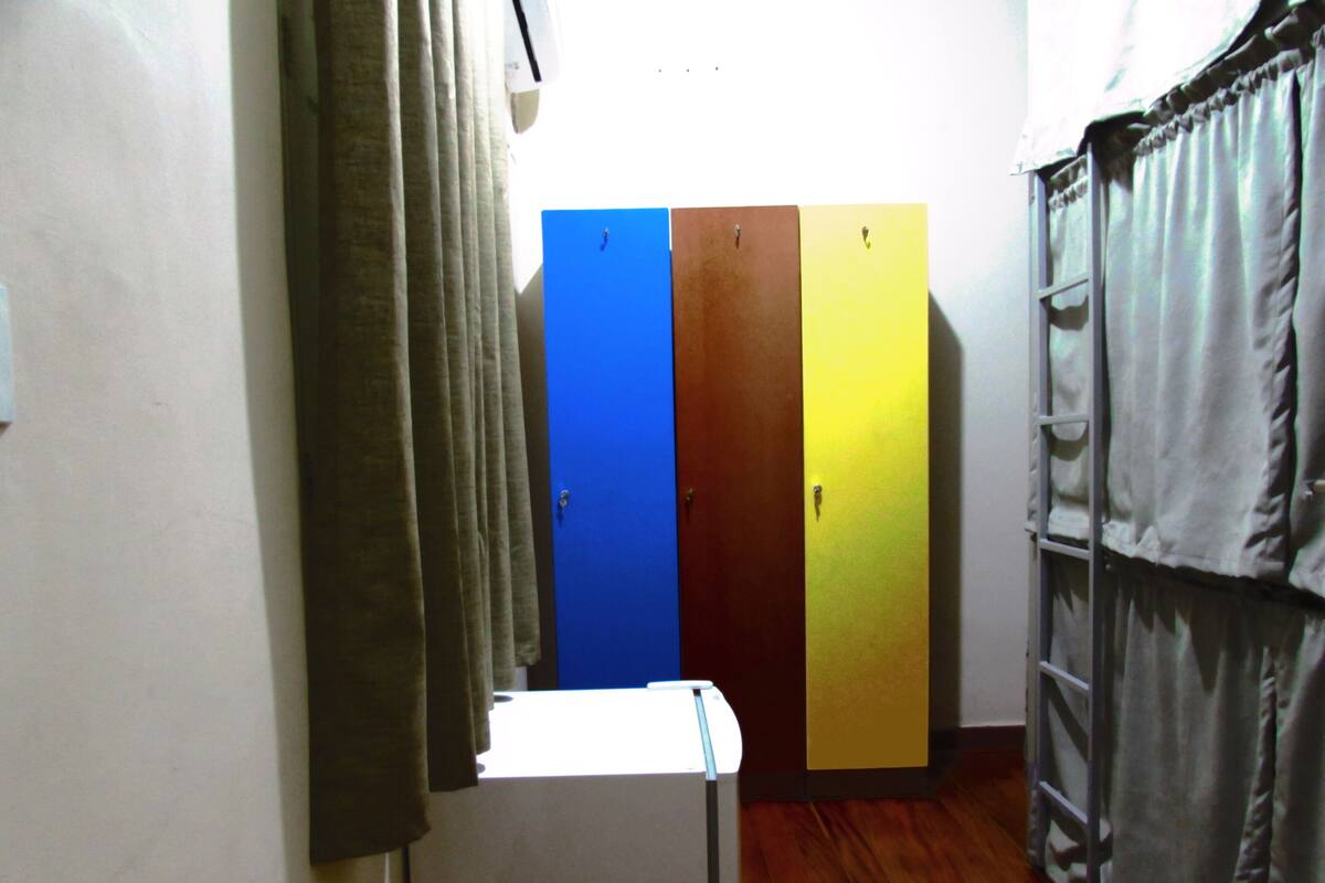 Un pasillo con un refrigerador blanco, puertas en azul, marrón y amarillo, y una cortina gris a la derecha.