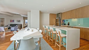 Una cocina moderna con una isla central, taburetes de bar y un comedor con mesa y sillas.