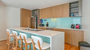 Una cocina moderna con una isla central, taburetes de bar, armarios de madera y un refrigerador de acero inoxidable.