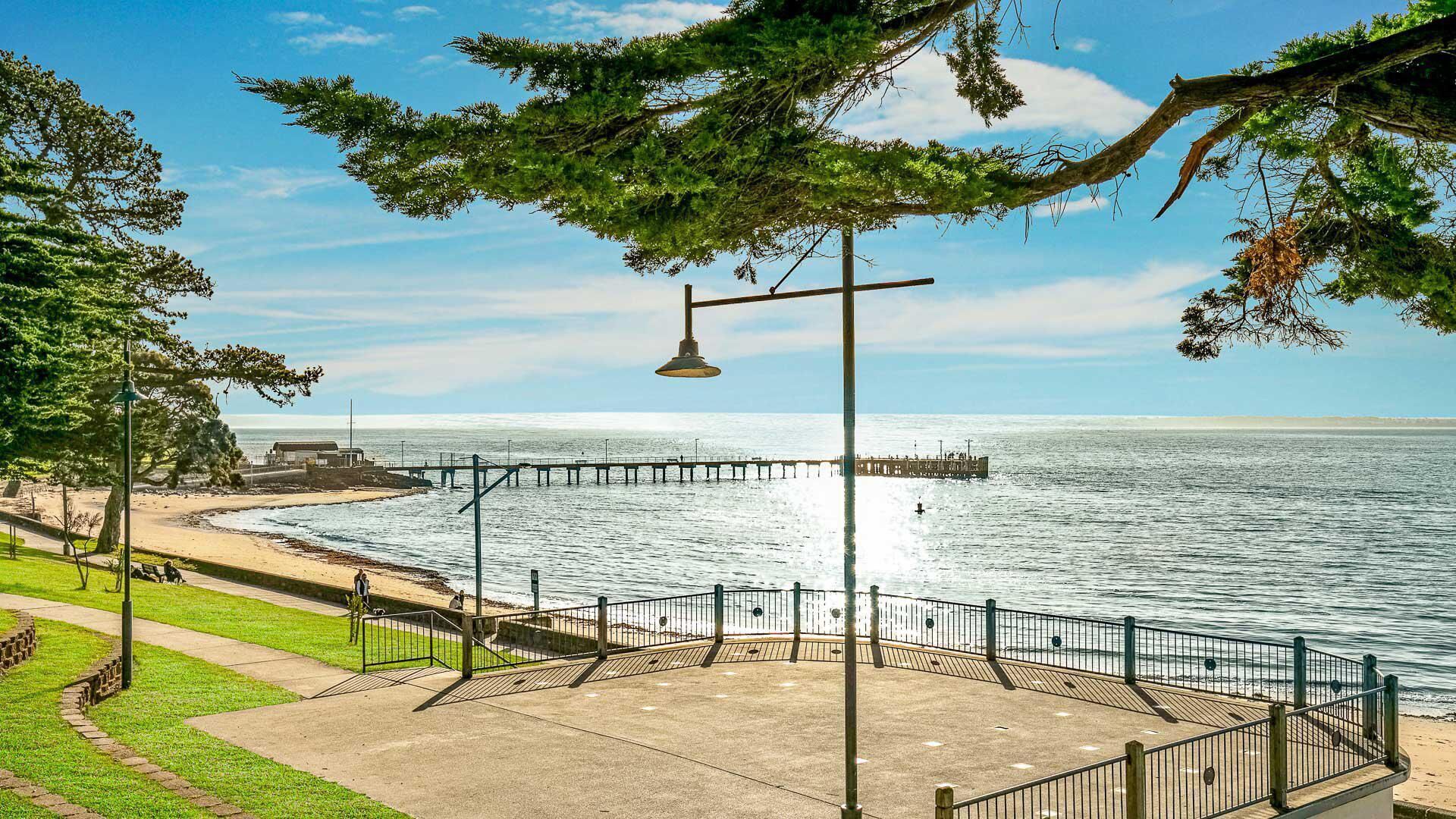 A coastal promenade with a wooden deck, metal railings, and a street lamp.