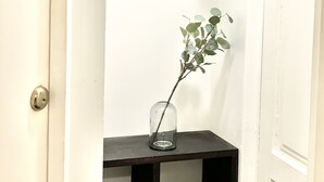 A narrow hallway with a door on the left, a small table with a vase and a branch, and a coat rack with hooks on the right. - City Home Finland Centrum Studio - Sauna (Tampere)