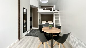 A compact room with a bunk bed, a round wooden table with four chairs, a hanging light fixture, and a radiator. - City Home Finland Centrum Studio - Sauna (Tampere)