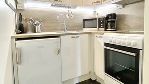 A compact kitchen with white cabinets, a built-in microwave, a coffee maker, and a small refrigerator. - City Home Finland Centrum Studio - Sauna (Tampere)