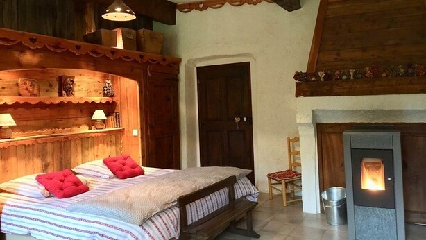 A cozy room with a bed, a wooden bench, a fireplace, and a shelf with decorative items. - SUITE ALPAGE (Méolans-Revel)